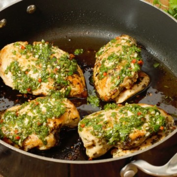 Pan seared chicken breasts topped with fresh chimichurri sauce in a pan