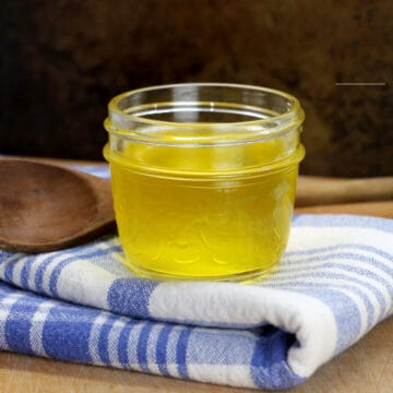 A small glass jar filled with golden clarified butter and displayed on a blue striped dish towel.