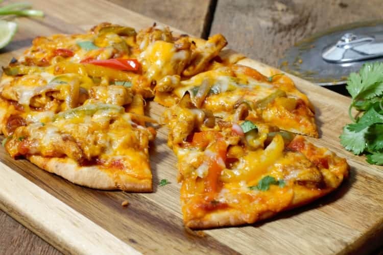 close up of a sliced chicken fajita naan pizza on a wooden serving board