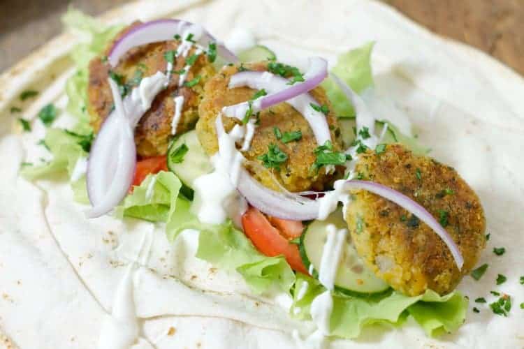 close up shot of falafel and various ingredients on a pita wrap