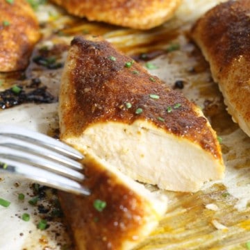 sliced open oven baked chicken breasts on a parchment lined sheet pan