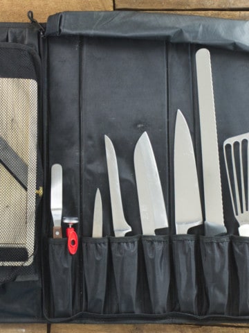 A knife roll filled with different types of kitchen knives on a wooden tabletop