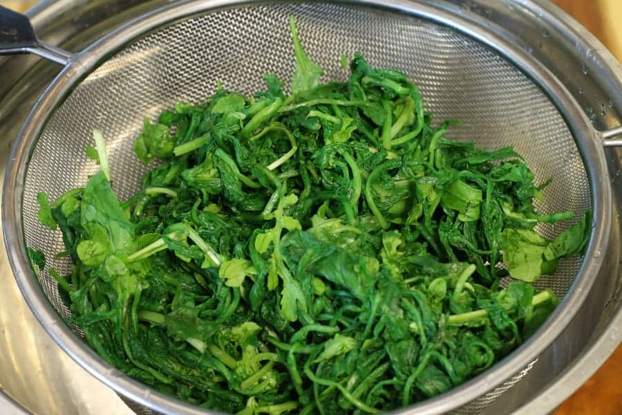 arugula in a sieve after squeezing out all the water from blanching