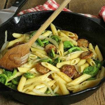 a simple fiddlehead and sausage penne pasta in a cast iron pan