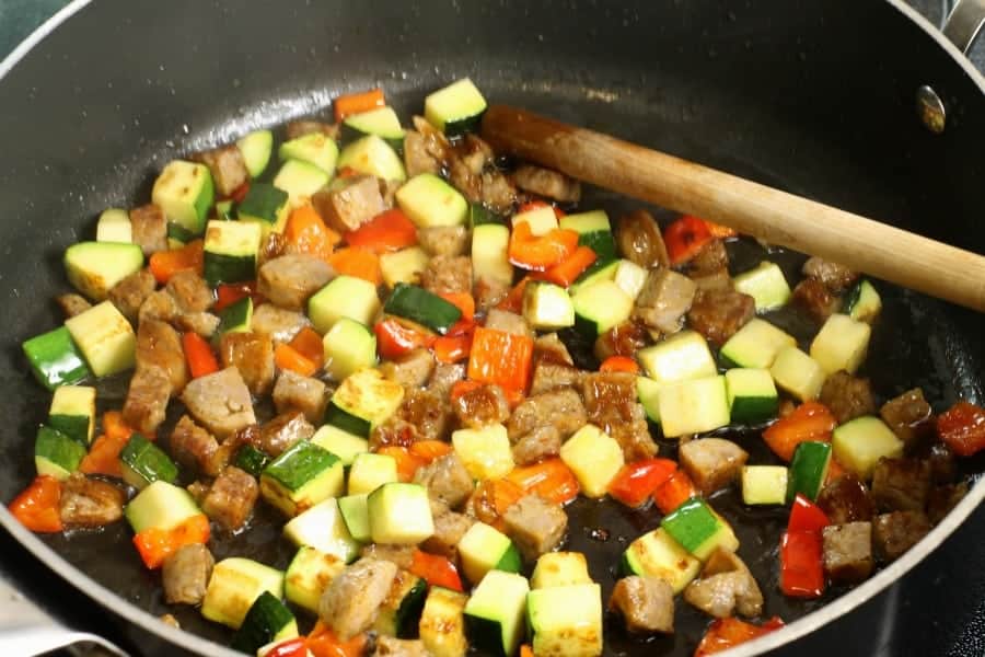 Diced sausage, zucchini, and red bell pepper being sauteed in a pan.