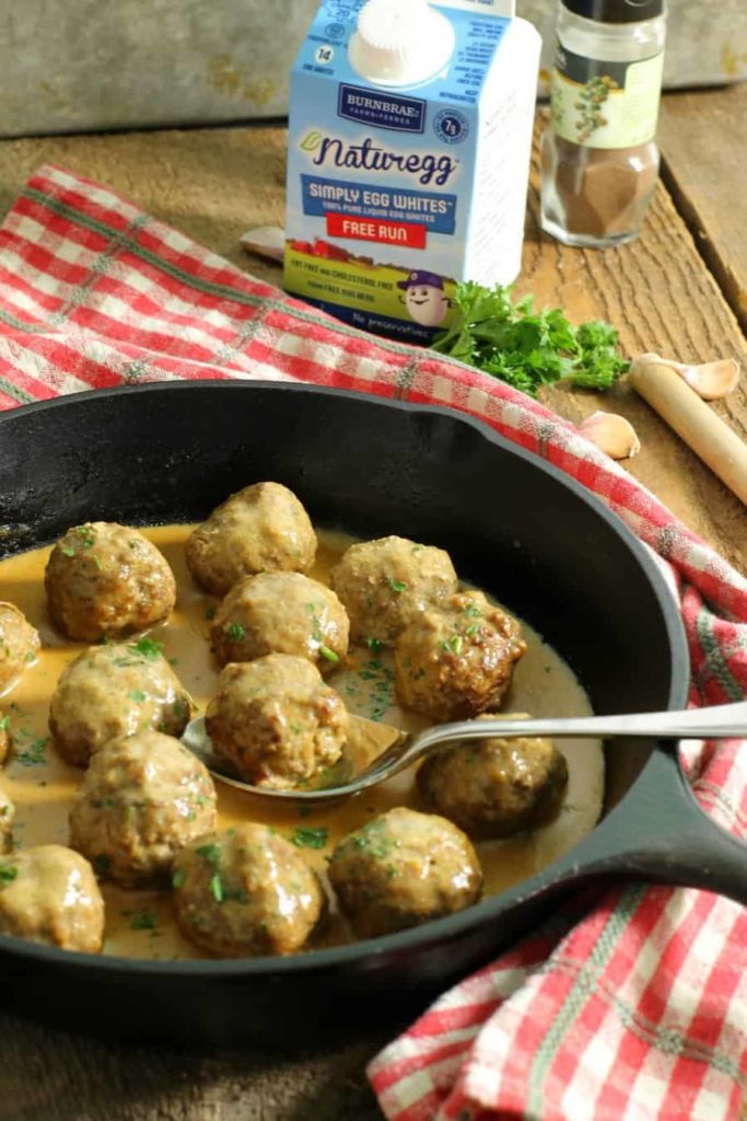 Gluten free swedish meatballs in a cast iron pan with a red checkered cloth wrapped around the handle.