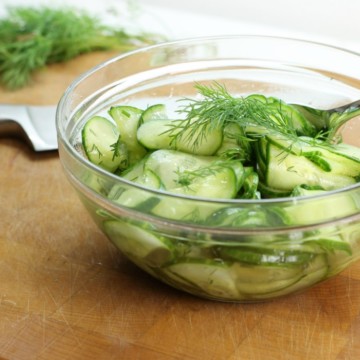 german cucumber salad garnished with dill in a glass bowl