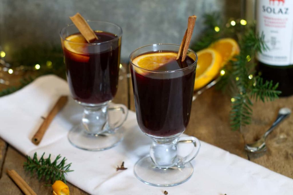 Two glass mugs filled with mulled red wine and garnished with cinnamon sticks and orange. 