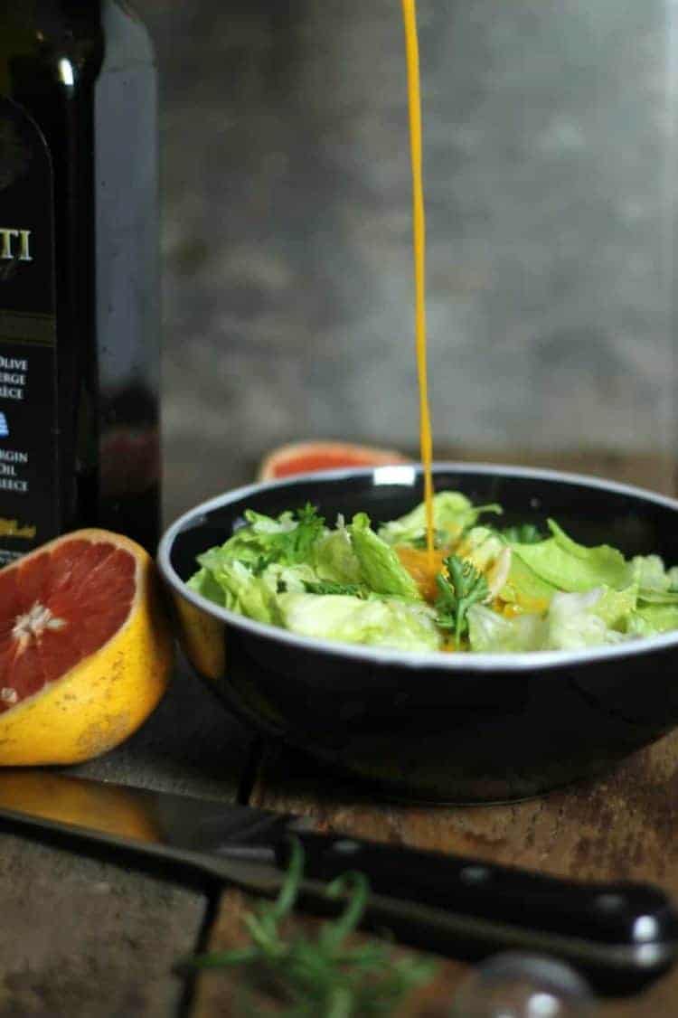 A stream of grapefruit vinaigrette being poured into a black bowl filled with salad greens