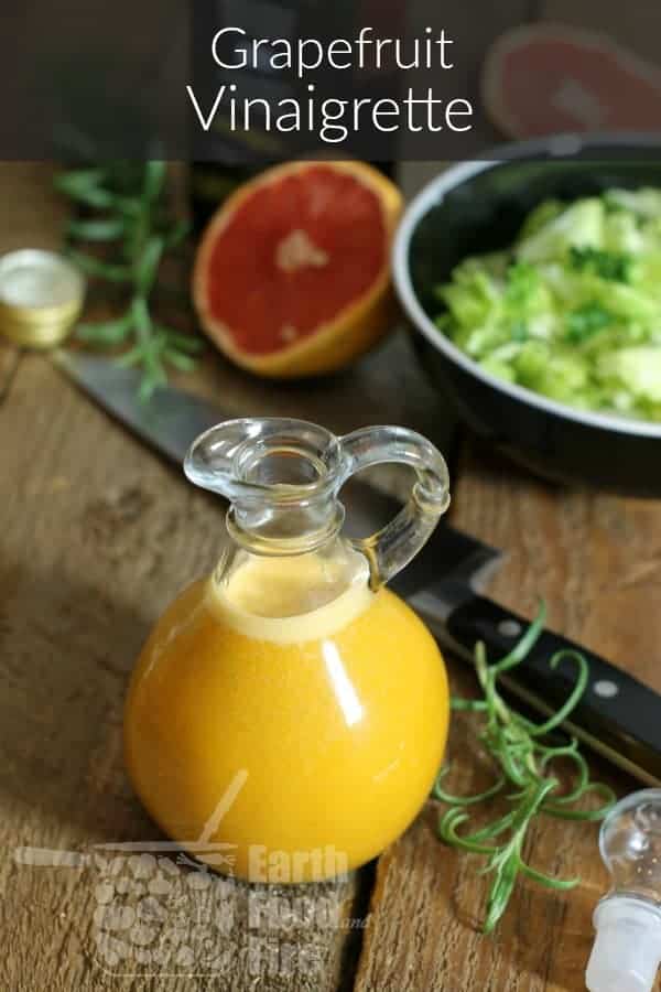 a glass jug of grapefruit vinaigrette on a rustic wood board table