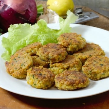 homemade falafel patties on a white plate surrounded by garnishes