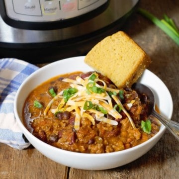 instant pot chili served in a white bowl and topped with shredded cheese and green onions