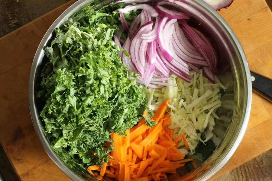 a top down view of kale slaw ingredients: shredded kale, green cabbage, carrot, and red onion in a bowl.