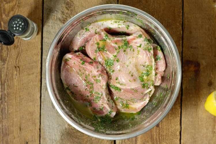 bone in pork chops marinating in a metal bowl