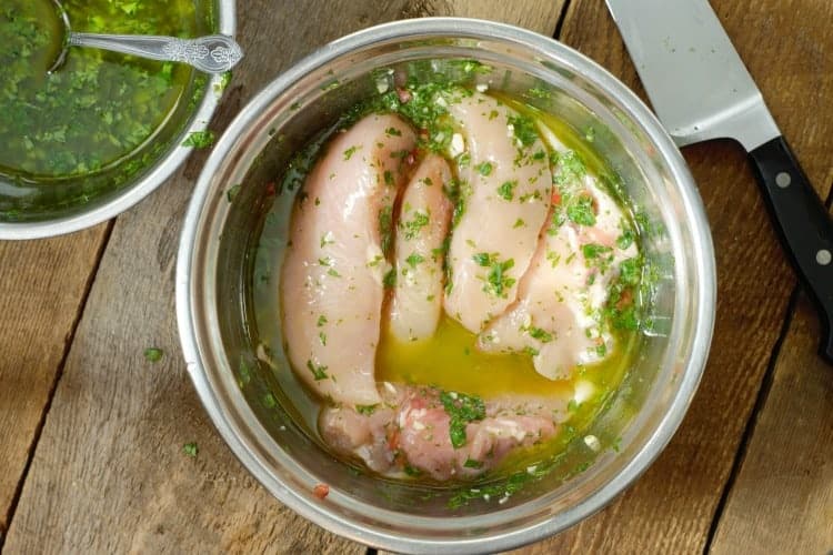 chicken breasts marinating in chimichurri in a steel bowl