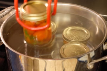 placing pickled cherry tomatoes in a hot water bath to can them