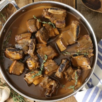 Top down view of red wine braised short ribs in a large pan on a wooden table top