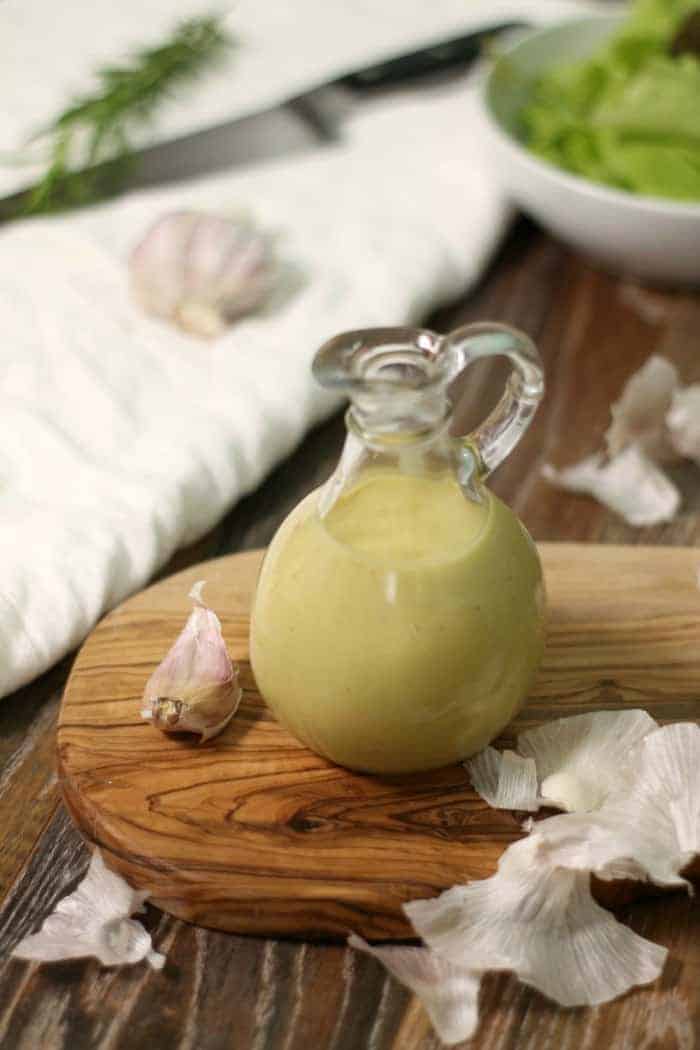 a glass bottle of homemade roasted garlic vinaigrette on a wooden serving board