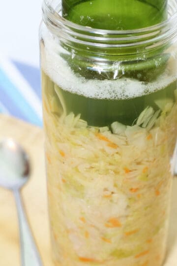 sauerkraut in a clear glass container starting to ferment.