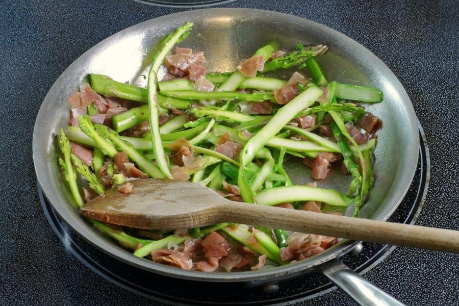 prosciutto and asparagus being sauteed in a pan