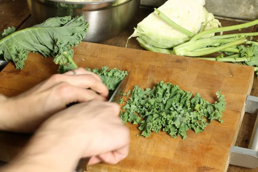 kale leaves being thinly shredded on a wooden cutting board