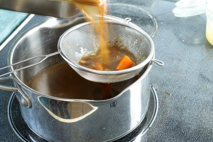 braising liquid being strained through a mesh strainer