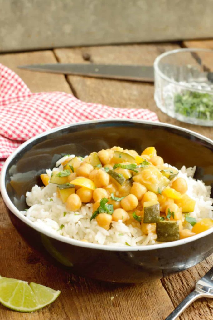 vertical image of chickpea curry served on top of basmati rice in a black porcelain bowl