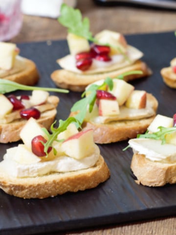 warm brie crostini's topped with a fresh apple and pomegranate salad on a black slate serving board